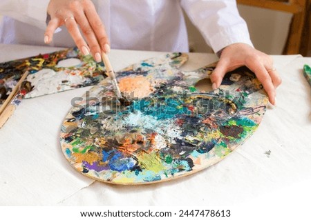 Oil color palette and brush in woman hand. Female artist painting process in studio, bright colorful palette with acrylic paint close up