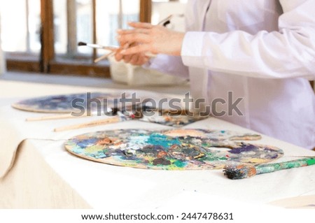 Oil color palette and brush in woman hand. Female artist painting process in studio, bright colorful palette with acrylic paint close up
