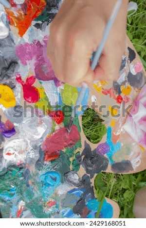 Oil color palette and human hand holding brush, artist painting proccess, bright colorful palette with acrylic paint close up
