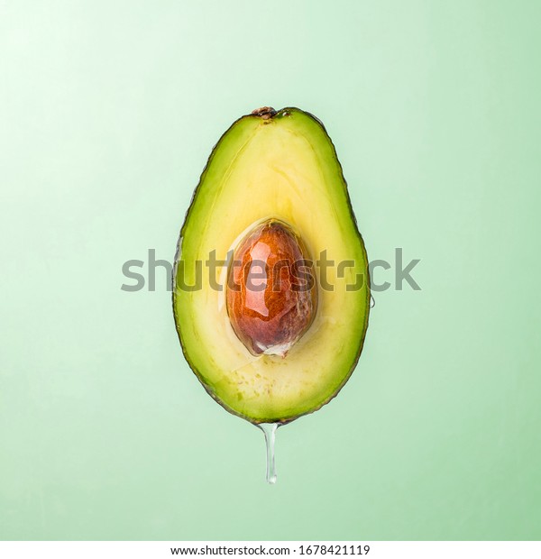 Oil\
dripping from sliced avocado on green\
background.