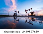 Oil field site, in the evening, oil pumps are running, The oil pump and the beautiful sunset reflected in the water, the silhouette of the beam pumping unit in the evening.