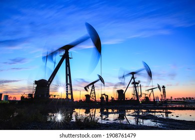 Oil field site, in the evening, oil pumps are running, The oil pump and the beautiful sunset reflected in the water, the silhouette of the beam pumping unit in the evening.