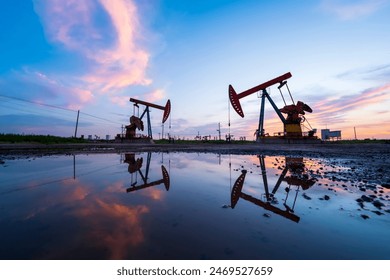 Oil field site, in the evening, oil pumps are running, The oil pump and the beautiful sunset reflected in the water, the silhouette of the beam pumping unit in the evening. - Powered by Shutterstock