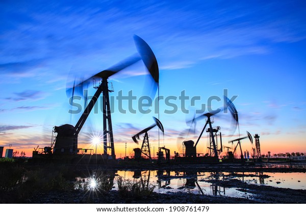Oil field site, in the\
evening, oil pumps are running, The oil pump and the beautiful\
sunset reflected in the water, the silhouette of the beam pumping\
unit in the evening.