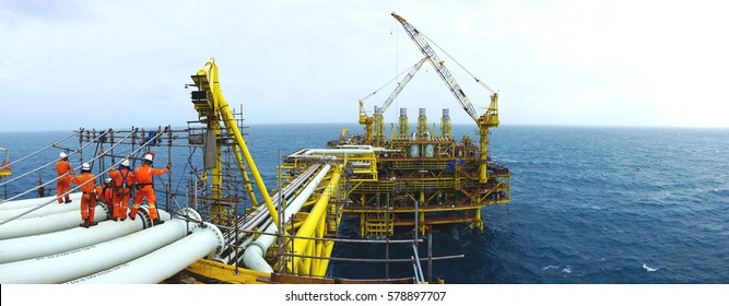 Oil and gas industries. Panorama view of offshore scaffolders standing on the pipeline and new oil and gas platform installed in the middle of the sea with cloudy sky background.