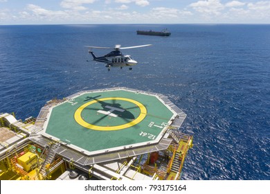 Oil and gas industry. A commercial helicopter landing on helideck at oil and gas platform in with backgroud open sea and tanker.