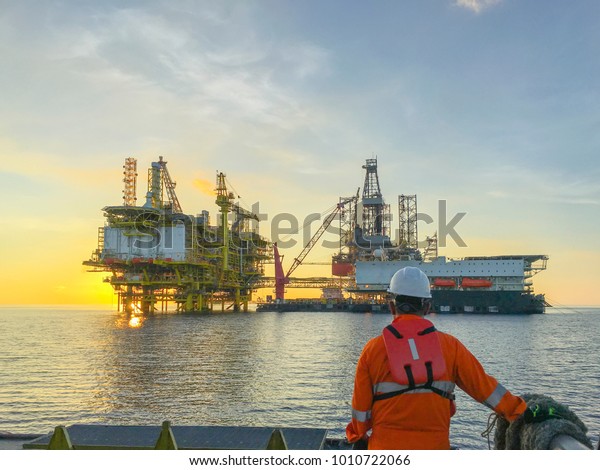 Oil and gas industry.\
Marine crew standing on supply vessel looking oil and gas platform\
during sunrise.