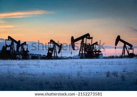 Oil and gas pump jacks working on a snow covered field at sunset in Rocky View County Alberta Canada.