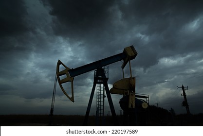 Oil And Gas Well Silhouette In Remote Rural Area, Profiled On Dramatic Warm Sky