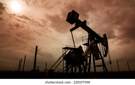 Oil And Gas Well Silhouette In Remote Rural Area, Profiled On Dramatic Warm Sky