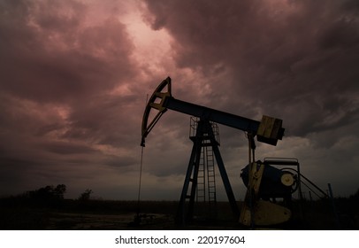 Oil And Gas Well Silhouette In Remote Rural Area, Profiled On Dramatic Warm Sky