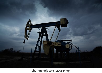 Oil And Gas Well Silhouette In Remote Rural Area, Profiled On Dramatic Warm Sky