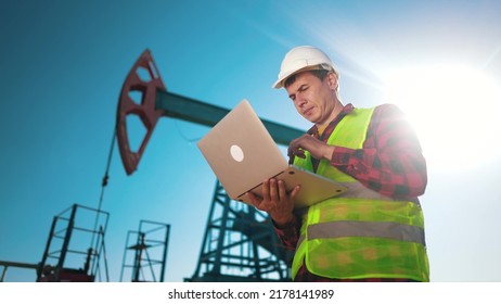 oil industry. engineer next to an oil rig. oil production business finance concept. gas production. a worker with a laptop monitors oil production next to an station. a worker in hard hat sun works