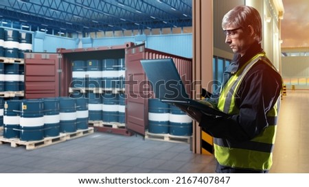 Oil logistics. Man with laptop next to warehouse. Blue barrels near container. Sea container for transportation of chemical products. Barrels of oil on pallets. Guy works in transport oil company