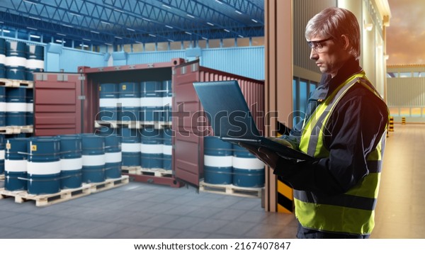Oil logistics. Man with laptop next to warehouse.
Blue barrels near container. Sea container for transportation of
chemical products. Barrels of oil on pallets. Guy works in
transport oil company