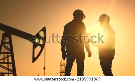 oil production. two silhouette workers work as a team next to an oil pump. business oil production production concept. two engineers of the oil and gas industry are discussing a business sun plan Stock fotó © 