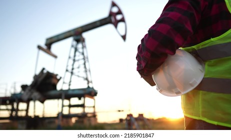 oil production. a worker holding a protective hard hat at sunset in the background an oil pump. oilfield business a extraction concept lifestyle. oil extraction pump. oil pump rig - Powered by Shutterstock