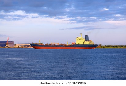 The Oil Products Tanker Is Anchored In A Port. The Huge Ice Breaker Is Drifting Near The Shore In The Background Of A Dramatic Sky.