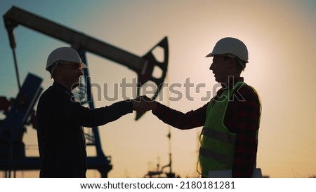 Oil pump. Engineers handshake. Corporate contract. People in helmets work at oil pump. Business contract handshake silhouette. Deposit of minerals. Working engineers teamwork in field at the oil pump