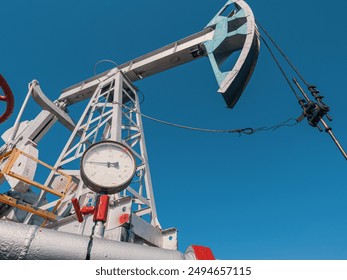 Oil pump jack operating under clear blue sky at oil field during daytime work hours - Powered by Shutterstock