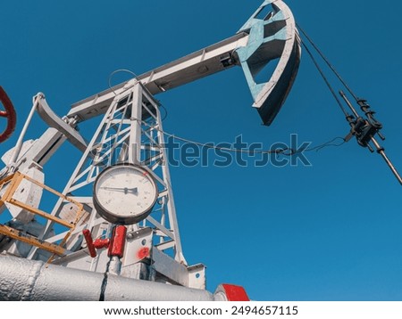 Oil pump jack operating under clear blue sky at oil field during daytime work hours