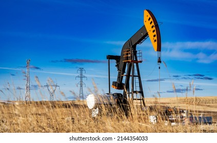 An Oil Pump Jack Working On An Agriculture Field With Oil And Gas Equipment And Distant Power Lines In Rocky View County Alberta Canada.