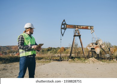 Oil Pump Worker Man Holding Digital Tablet Resources Field. Manager Engineer Man Work On Digital Tablet Beside Pumping Oil Unit