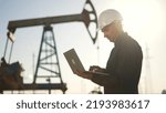 Oil pump.Engineer work with laptop and diagram.Checking operation of oil pump at plant.Silhouette of man in an industrial area.Silhouette of an engineer checking operation of an oil pump in desert