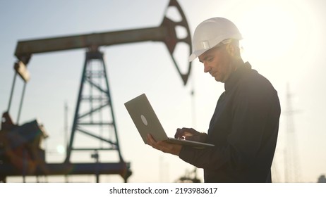 Oil pump.Engineer work with laptop and diagram.Checking operation of oil pump at plant.Silhouette of man in an industrial area.Silhouette of an engineer checking operation of an oil pump in desert - Powered by Shutterstock