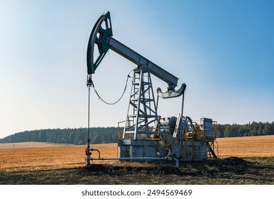 Oil pumpjack in operation amidst yellow fields under clear blue sky during daylight hours