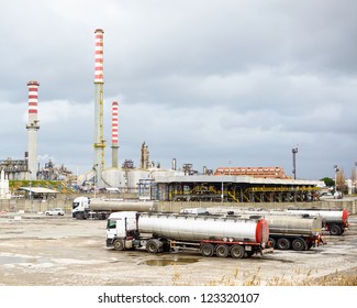 Oil Refinery Industry, Smoke Stacks And Silver Tanker Lorry Or Truck In Parking