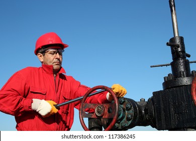 Oil Rig Valve Technician at Work. Oil and Gas Industry.
Oil worker wearing red coveralls and red helmet, working at pump jack oil well.
