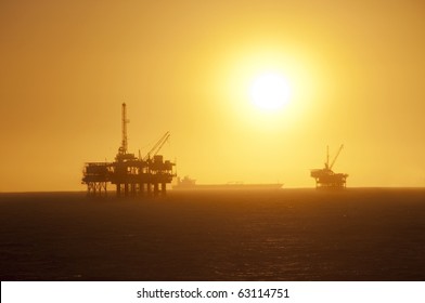 Oil Rigs in the ocean, ship passing by and a beautiful sunset in Huntington Beach, California.