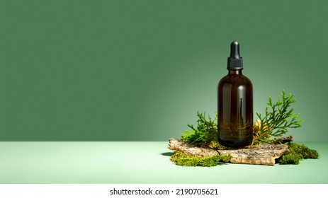 Oil with serum for skin and hair care. A concept of essential oil, moss and tree bark on a green background. Glass brown bottle of body oil with a dropper. Self-care and wellness. Copy space. Banner. - Powered by Shutterstock