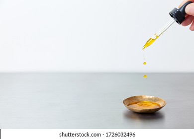 Oil Serum Tincture Droplets Squeezed From Dropper Into Brass Gold Bowl On Stainless Surface