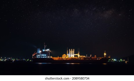 Oil ship tanker loading oil at the oil brige on the sea from refinery for transportation. at night over lighting and starlight background process 