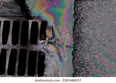 An oil slick against the backdrop of an asphalt road flows into a storm drain through a grate. Environmental problems of water pollution. - Powered by Shutterstock