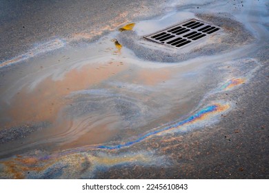 Oil slick on the asphalt road background drains into the storm drain. Water pollution environmental problems. Selective focus.