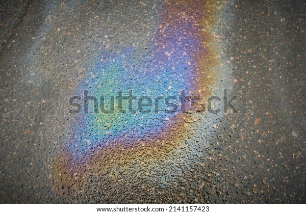 Oil slick on the\
asphalt road background. Rainbow gasoline oil spill on the pavement\
as a texture or background.