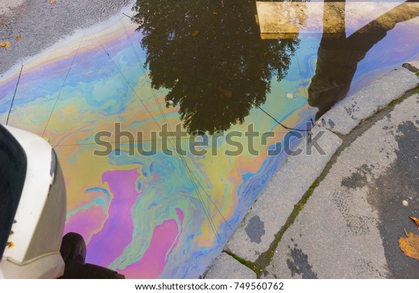 Oil stain,\
Gas Stain drop from the Car on the asphalt with human at\
reflection. Symbol of pollution in big\
cities.