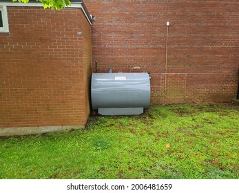 An Oil Tank Hidden On The Side Of A Suburban House In A Close Knit Community. The Tank Is Painted Gray.