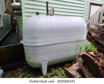 An Oil Tank Hidden On The Side Of A Suburban House In A Close Knit Community. The Tank Is Painted Gray And Nestled Next To Vegetation.