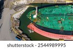 Oil tanker in filled drydock. Water flushing from anchor hawser pipe. Aerial view focused on bow.