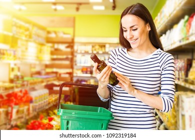 Oil for vegetable salad. Beautiful smiling young woman in casual clothes is holding a bottle of olive oil in the supermarket. - Powered by Shutterstock