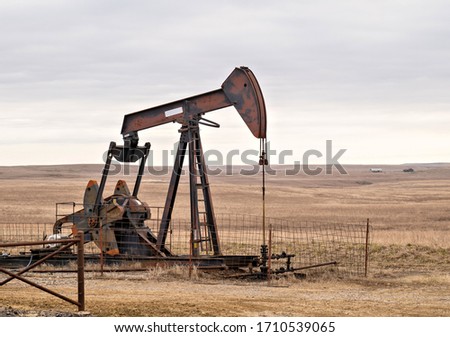 Oil Well Pump Jack pumping crude oil for fossil fuel energy. American Petroleum Oil and Gas Industry equipment extracting from a field on a prairie in the United States of America.
