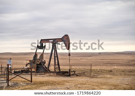 An oil well pump jack pumping on the prairie of Oklahoma during a cloudy day.