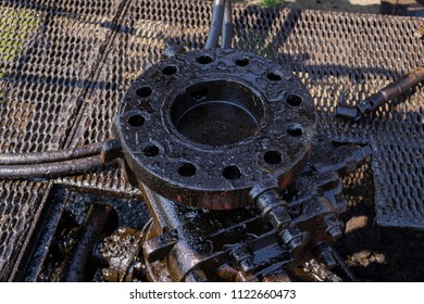 Oil Well And Small Crude Lake At The Well Head, Crude Oil From Well With Reflex Of Pumpjack. Blowout Preventer Device With Flanges On The Oil Rig