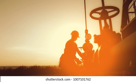 Oil worker is checking the oil pump on the sunset background. - Powered by Shutterstock