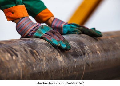 Oil Worker Hands In Green And Orange Work Wear And Working Gloves And Rusted Drilling Pipe. Works On Oil Deposit In Kazakhstan.  Close-up