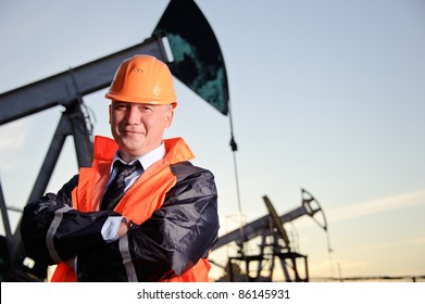 Oil worker in orange uniform and helmet on of background the pump jack and sunset sky.